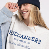 Person wearing a white sweatshirt with 'Buccaneers' text, blue beanie, and denim jacket on a light gray background