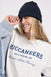 Person wearing a white sweatshirt with 'Buccaneers' text, blue beanie, and denim jacket on a light gray background