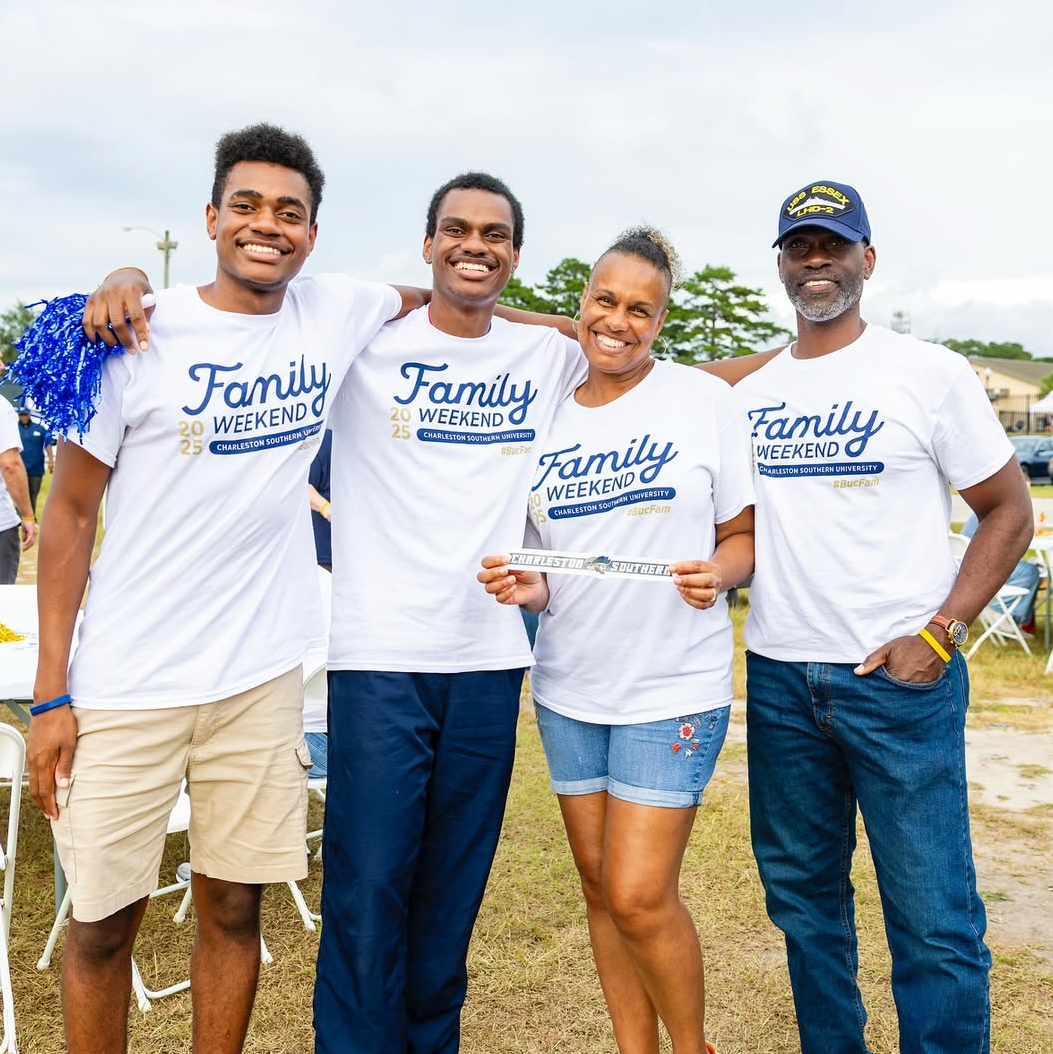 Four people wearing 'Family Weekend' shirts standing together outdoors.