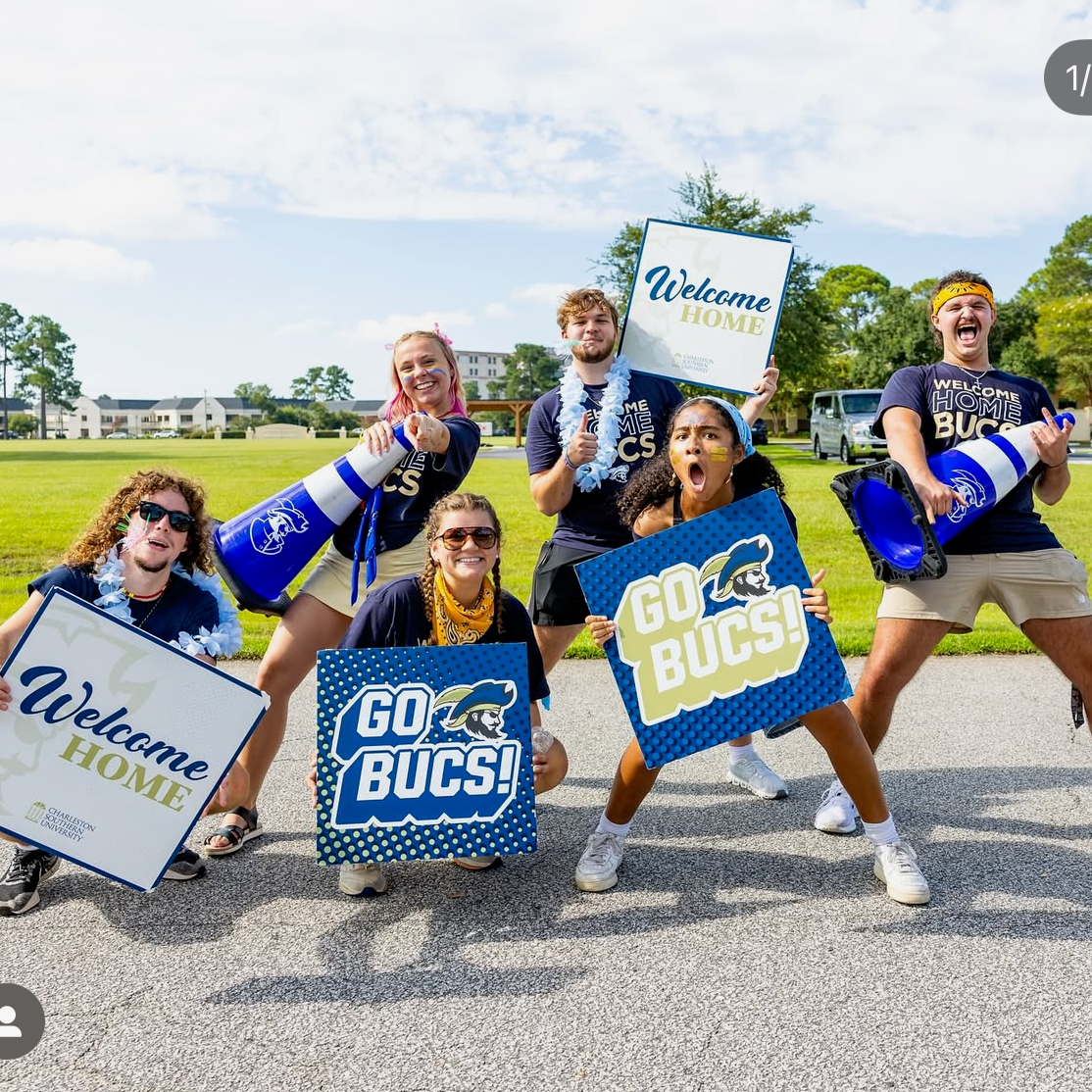 Group of people holding 'Welcome Home' and 'Go Bucs!' signs outdoors.